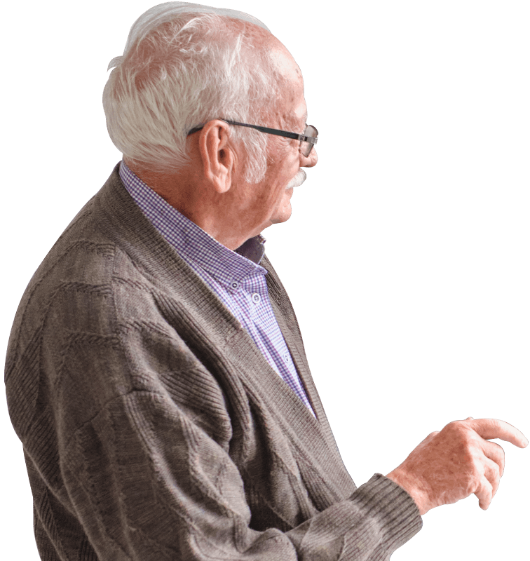 Elderly man with white hair and glasses, wearing a brown cardigan and purple checkered shirt, gesturing thoughtfully to the side against a black background.